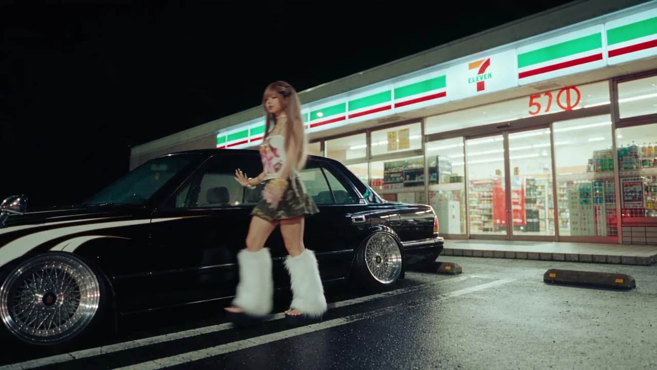 The 7-Eleven walk. The camera, the car's angle and her path come from the blockout; the store, the neon and the wet asphalt come from words.